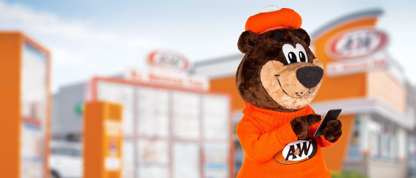Rooty the Great Root Bear texting on a phone in front of an A&W Restaurant